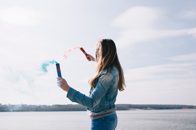 Long haired woman holding colored smoke torches