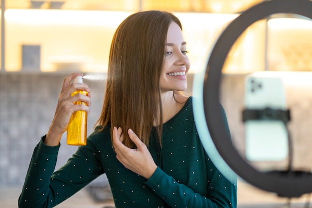 Free photo long-haired woman spraying hairspray on her hair and smiling