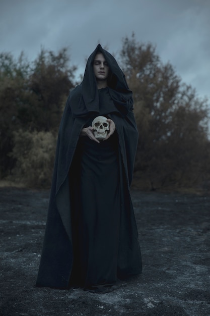 Free photo long portrait of a man dressed as dark mage with skull