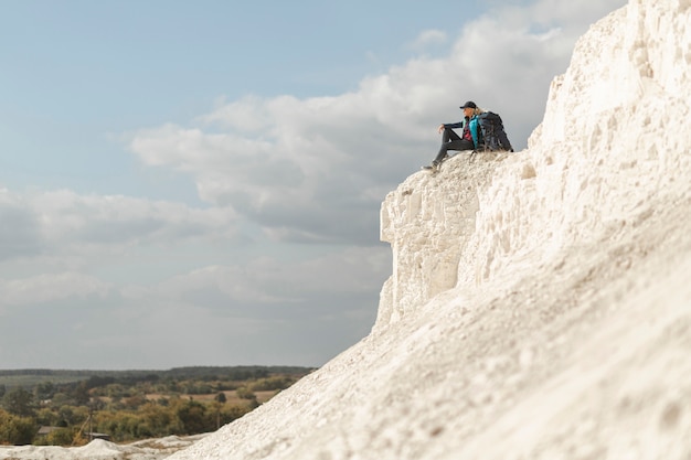 Free photo long shot traveler sitting on the mountain