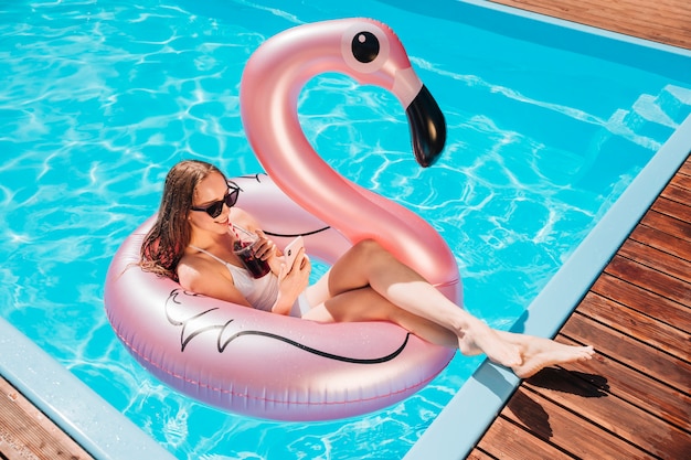 Free Photo long shot woman having a drink in swim ring