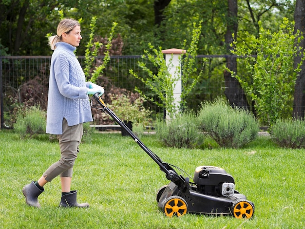 Long shot woman mowing the yard