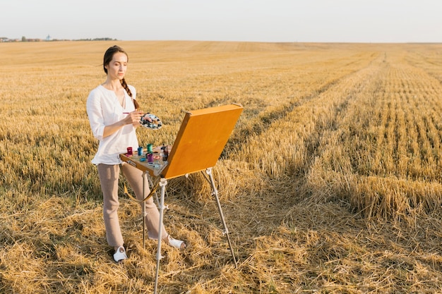 Free photo long shot woman painting in the nature