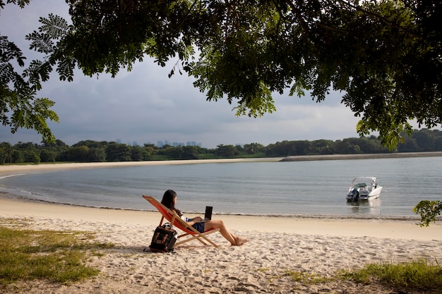 Long shot woman working on laptop at beach