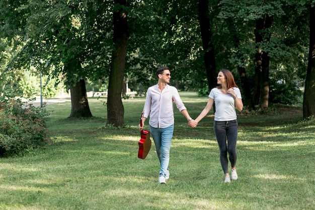 Free photo long shot young couple walking through meadow hand in hand