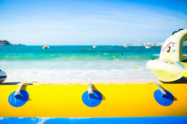 Look over blue and yellow air tube at foaming sea waves under sunny sky