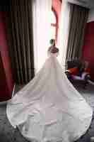 Free photo look from behind at bride with long dress standing before the window