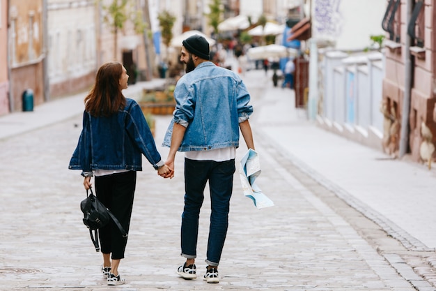 Free Photo look from behind at the couple of tourists holding their hands together while walking around the city