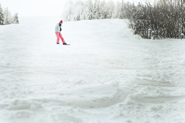 Look from below at lady in blue ski jacket going down the hill on her snowboard 