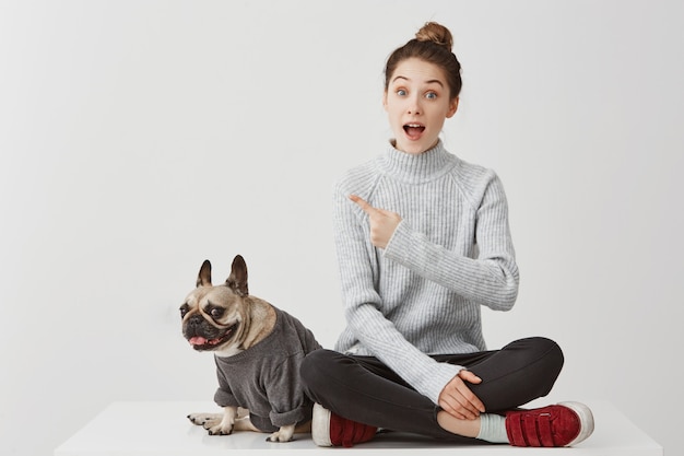 Free Photo look there! surprised woman pointing index finger asking for paying attention on something worthy. female model gesturing meaning this is cool in company of dog. lifestyle concept, copy space