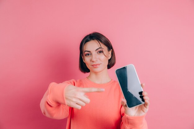 Look at this cell phone! Pleased happy woman points with index finger at blank screen, shows modern device, happy surprised emotions.