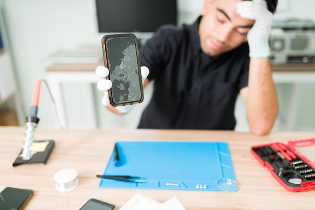 Free photo look at this ugly smartphone. upset male technician feeling worried while showing the cracked screen of a new smartphone