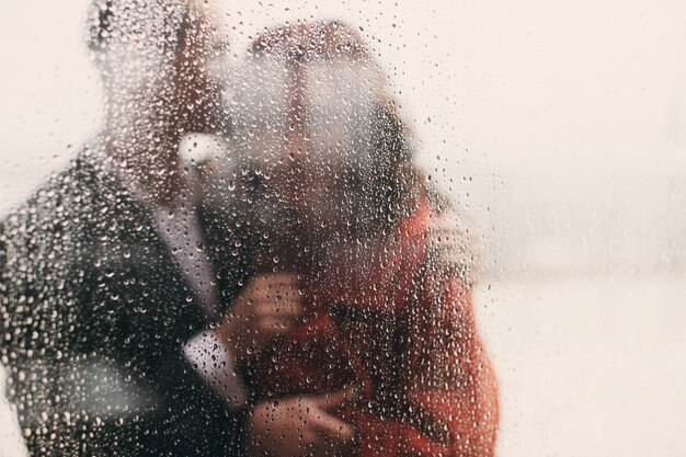 Look throught the wet window at hugging couple