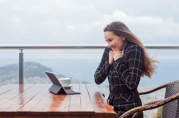 Looking at laptop computer screen blogger girl is feeling happy by holding hands on chest by sitting on city view background