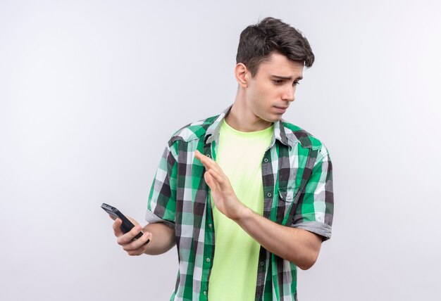 Looking at side caucasian young man wearing green shirt doesn't look a phone call on isolated white wall