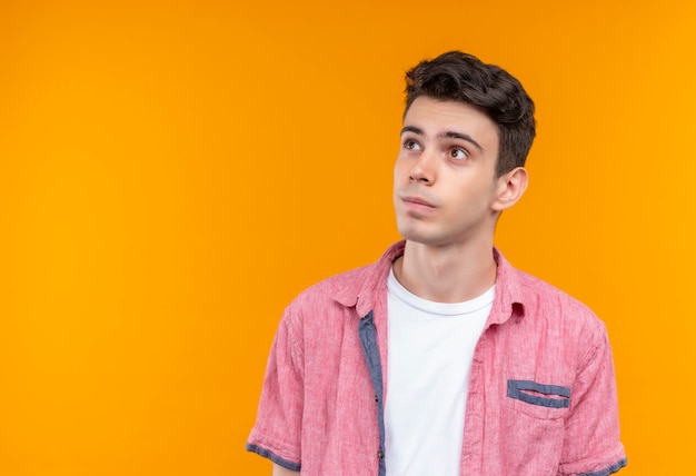 Looking at side caucasian young man wearing pink shirt on isolated orange wall