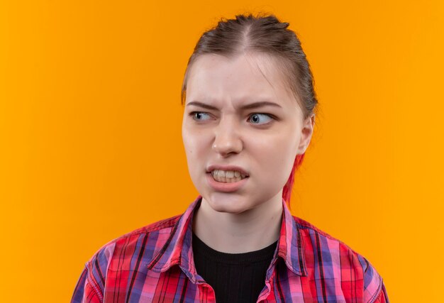 Looking at side confused young beautiful woman wearing red shirt on isolated yellow wall