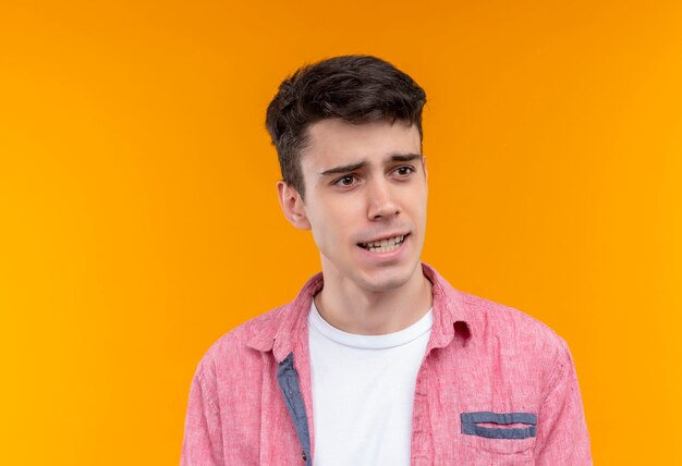 Looking at side thinking caucasian young man wearing pink shirt on isolated orange wall