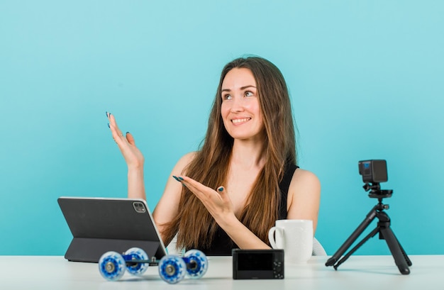 Looking up blogger girl is posing by pointing up with hands on blue background