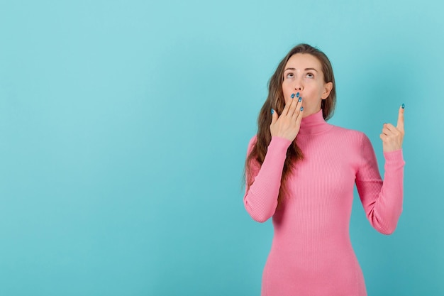 Looking up blonde girl is holding hand on mouth on blue background