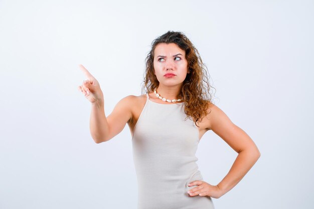 Looking up girl is pointing up with forefinger and putting other hand on waist on white background