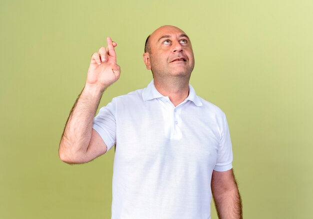 Looking at up pleased mature man crossing fingers isolated on olive green wall