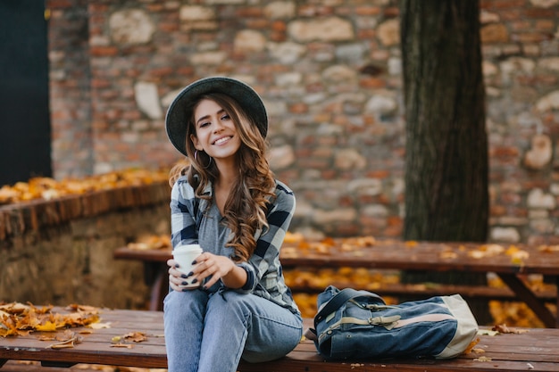 Free photo lovable european female model wears casual jeans and blue shirt sitting outdoor in warm october weekend