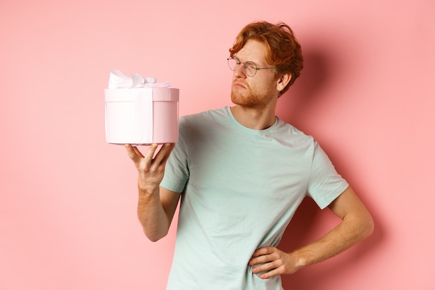 Free photo love and holidays concept intrigued redhead guy looking puzzled at gift box dont know what inside st...