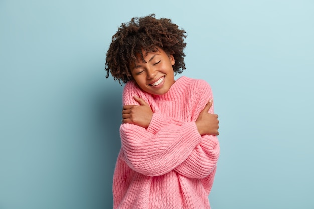 Free photo love yourself concept. photo of lovely smiling woman embraces herself, has high self esteem, closes eyes from enjoyment