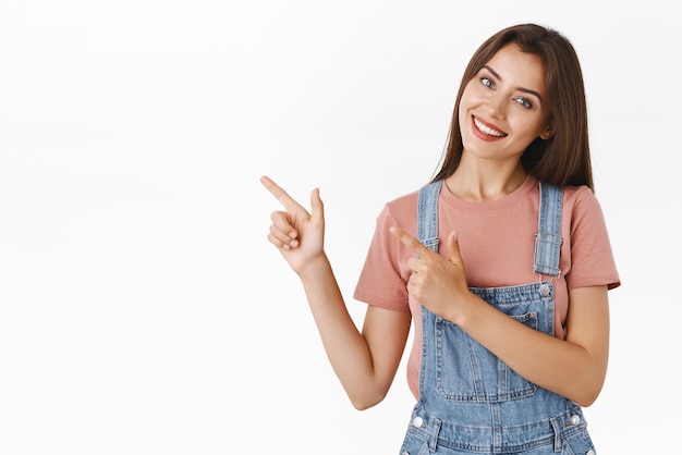 Lovely alluring cheerful beautiful woman in dungarees tshirt tilt head silly and smiling as promote company product pointing upper left corner give advice to check out cool advertisement