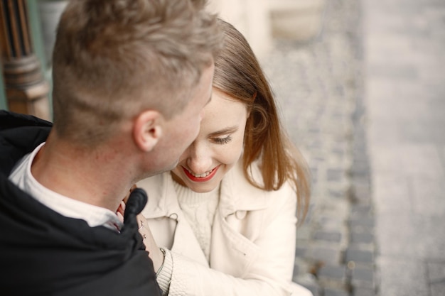 Free photo a lovely couple hugging and kissing in the street on autumn time man kissing his girlfriend in a forehead girl wearing beige coat and man black jacket