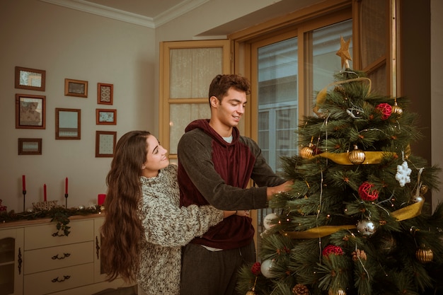 Lovely couple hugging while decorating Christmas tree