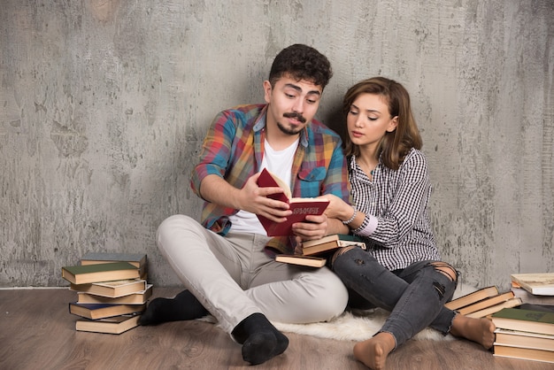 Free photo lovely couple reading an interesting book while sitting on floor