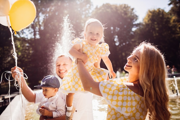 Free photo lovely family dressed in the same clothes sits on the fountain with their children and yellow balloons