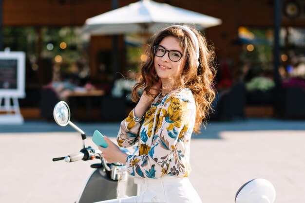 Lovely girl with beautiful dark-brown hair looking with interest while waiting friend in front of cafe