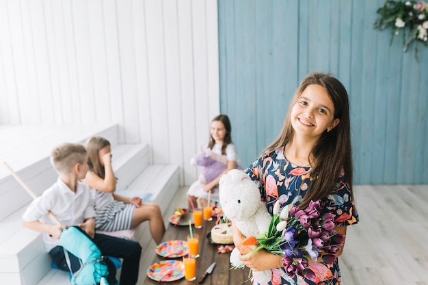 Lovely girl with toy and flowers on birthday party