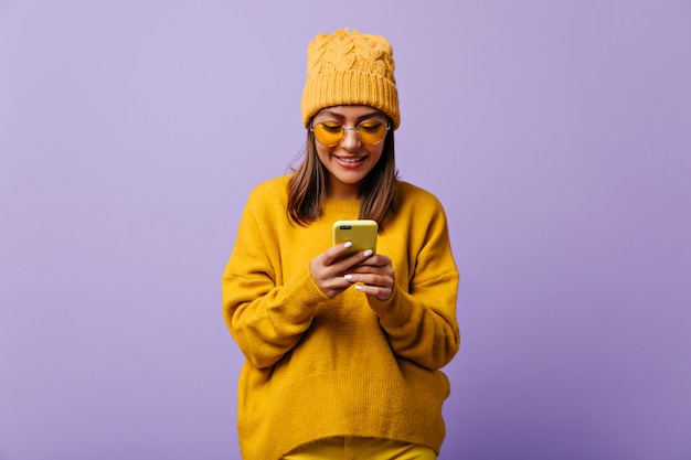 Free photo lovely glad woman likes yellow color and wears total yellow outfit. snapportrait of beautiful girl chatting in her smartphone