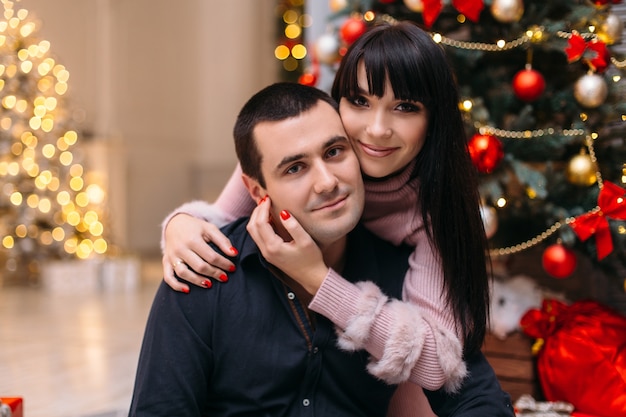 Lovely happy young couple poses before a red Christmas tree in a cosy corner