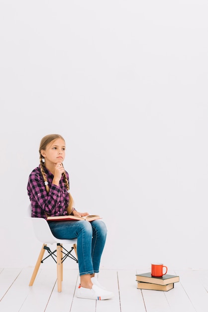 Free photo lovely little girl sitting on a chair reading a book