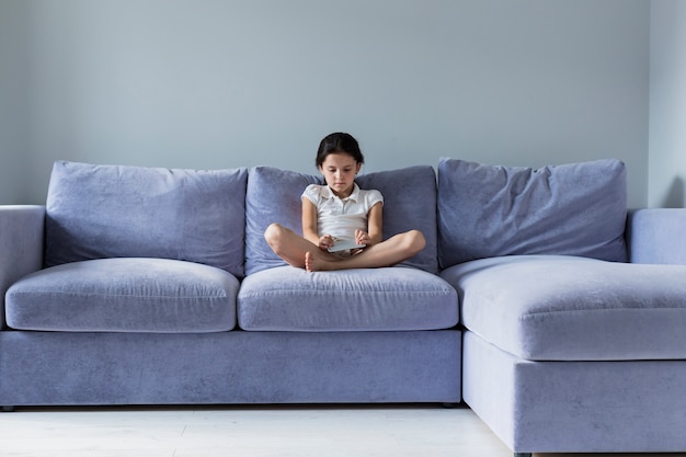 Free photo lovely little girl with smartphone on the sofa