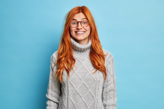 Free photo lovely redhead young woman with european appearance smiles pleasantly dressed in warm sweater expresses positive emotions hears good news.