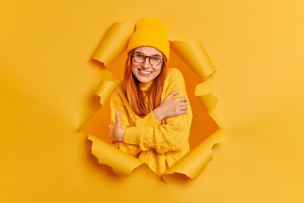 Free photo lovely smiling redhead woman embraces herself feels comfort wears warm knitted sweater looks gladfully.