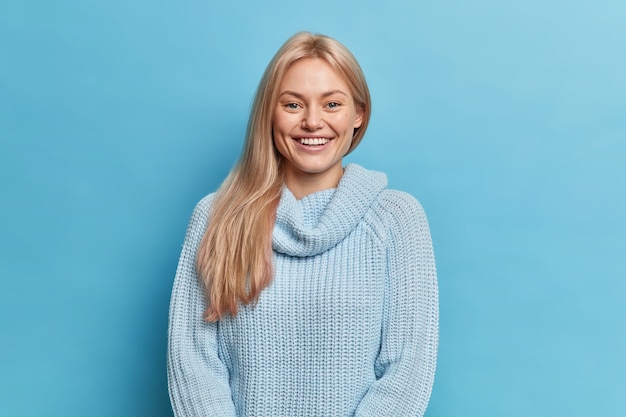 Free photo lovely smiling young woman with blonde hair expresses positive emotions has perfect white teeth dressed in knitted warm jumper