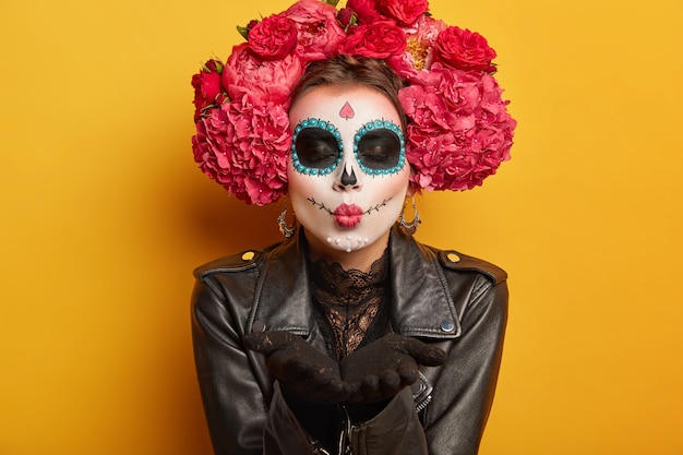 Free photo lovely woman blows mwah, keeps lips folded, wears creative makeup, prepares for carnival, prepares for day of dead