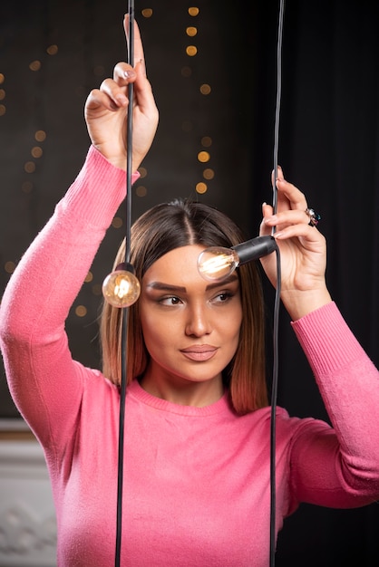 A lovely woman in sweater posing near light lamps . 