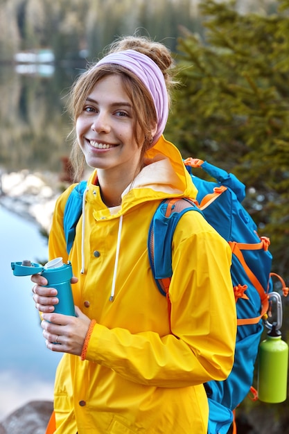 Free Photo lovely woman with glad facial expression, dressed in yellow raincoat, carries rucksack