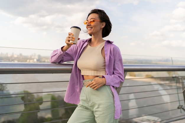 Lovely woman with short hairstyle walking on modern bridge in windy summer day