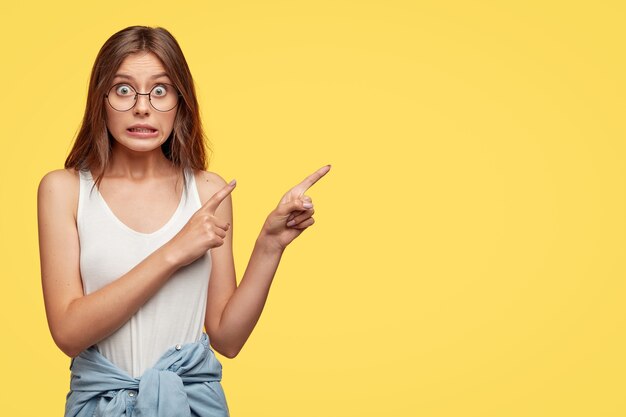 Lovely young brunette with glasses posing against the yellow wall