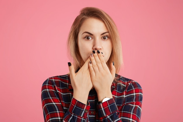 Free Photo lovely young female tries to keeps silence, not gossip and tell confidential information covered her mouth with her hands