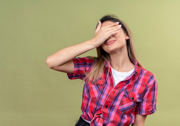 Free photo a lovely young woman in a checked shirt covering eyes with hand on a green wall